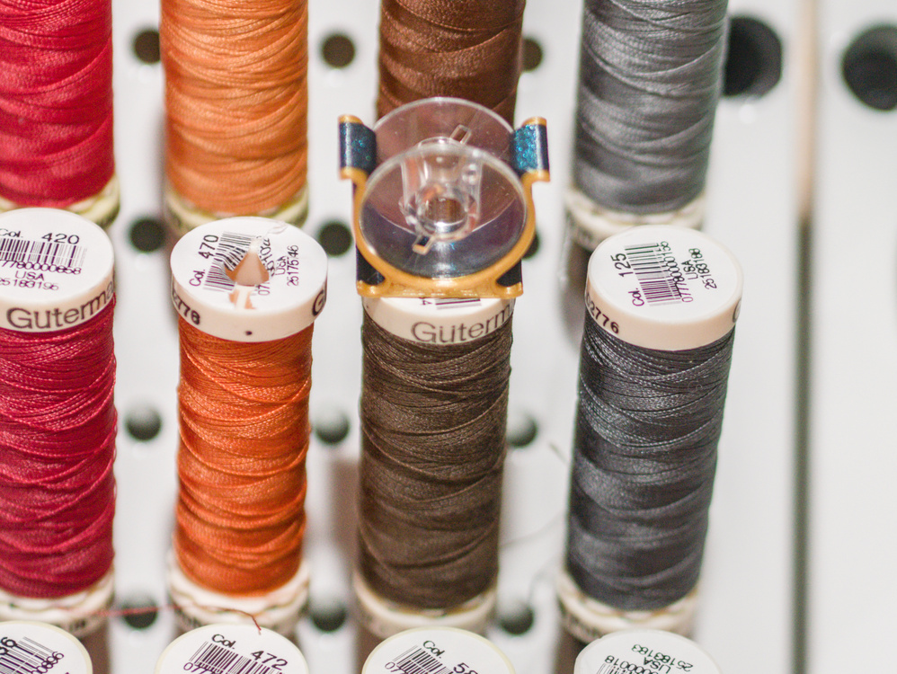 Bobbin keeper clipped onto a spool of thread on a wall rack